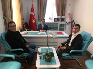 Fotoğrafta bir ofis ortamı görülüyor. Ortada bir masa var ve masanın arkasında takım elbise giymiş Hüseyin KURTAY oturuyor. Masanın sol tarafında siyah ceket giymiş Oğuz ÖZDEMİR, sağ tarafında ise beyaz kapüşonlu bir üst ve siyah ceket giymiş Mert YAKIŞTIR oturuyor. Masanın üzerinde birkaç dosya ve bir fincan kahve bulunuyor. Masanın arkasında Türk bayrağı ve Genel Müdürlüğün bayrağı da var. Ayrıca, duvarda Atatürk'ün bir fotoğrafı ve birkaç plaket yer alıyor. Masanın önünde bir saksıda orkide çiçeği var. Sağ tarafta ise "Sivil Toplum İlişkileri Genel Müdürlüğü" yazılı bir pankart görülüyor.